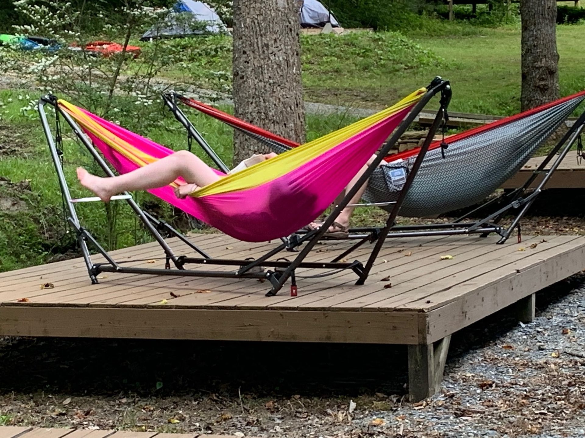 Person relaxing in a pink hammock on a wooden deck in a grassy park area