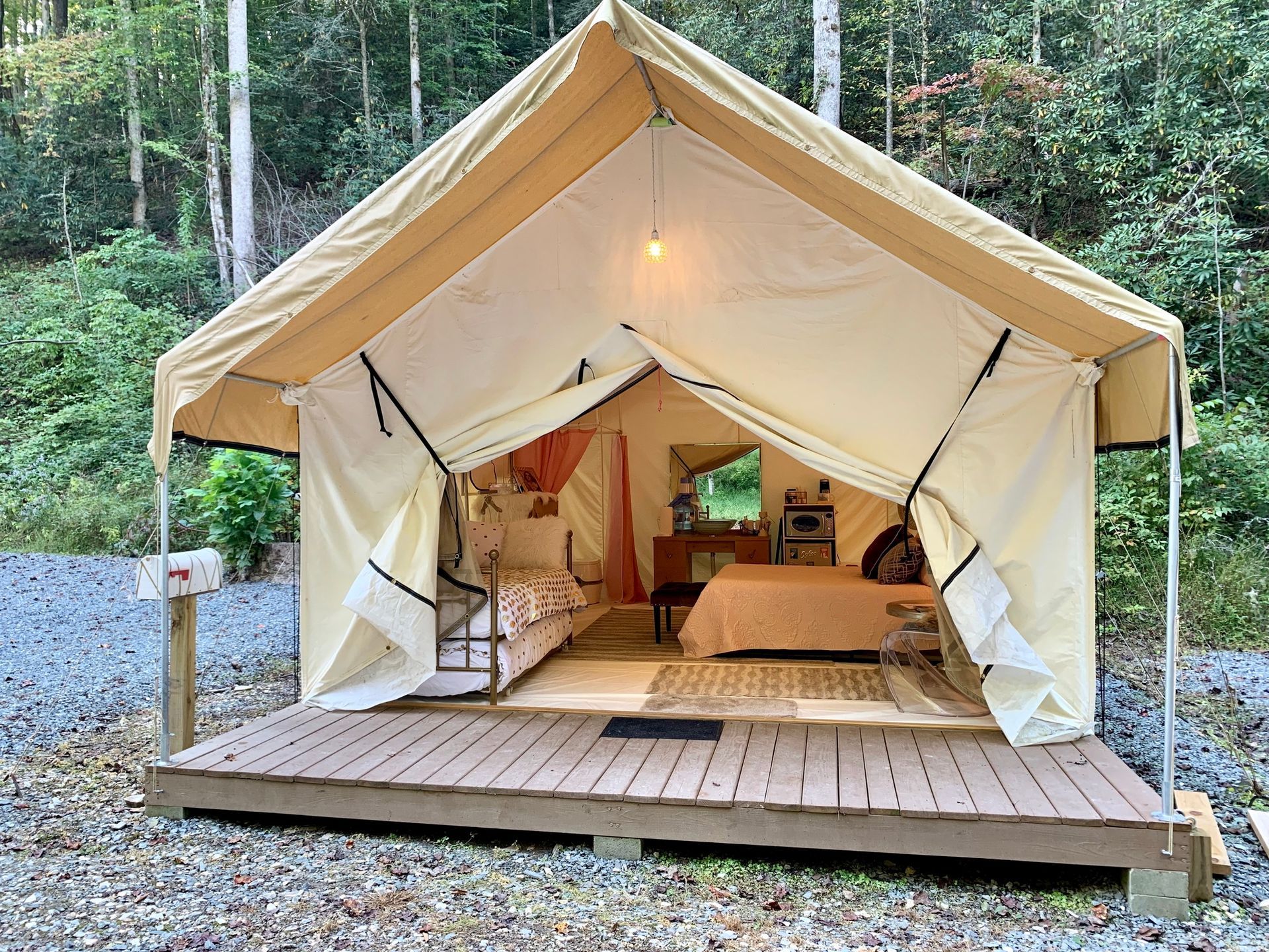 Open glamping tent with wooden deck, lit interior, and forest backdrop
