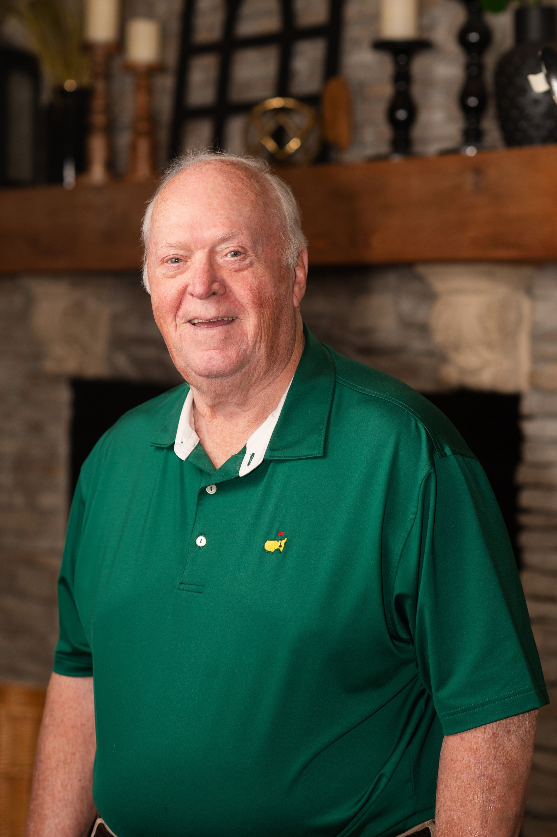 A man in a green shirt is standing in front of a fireplace.