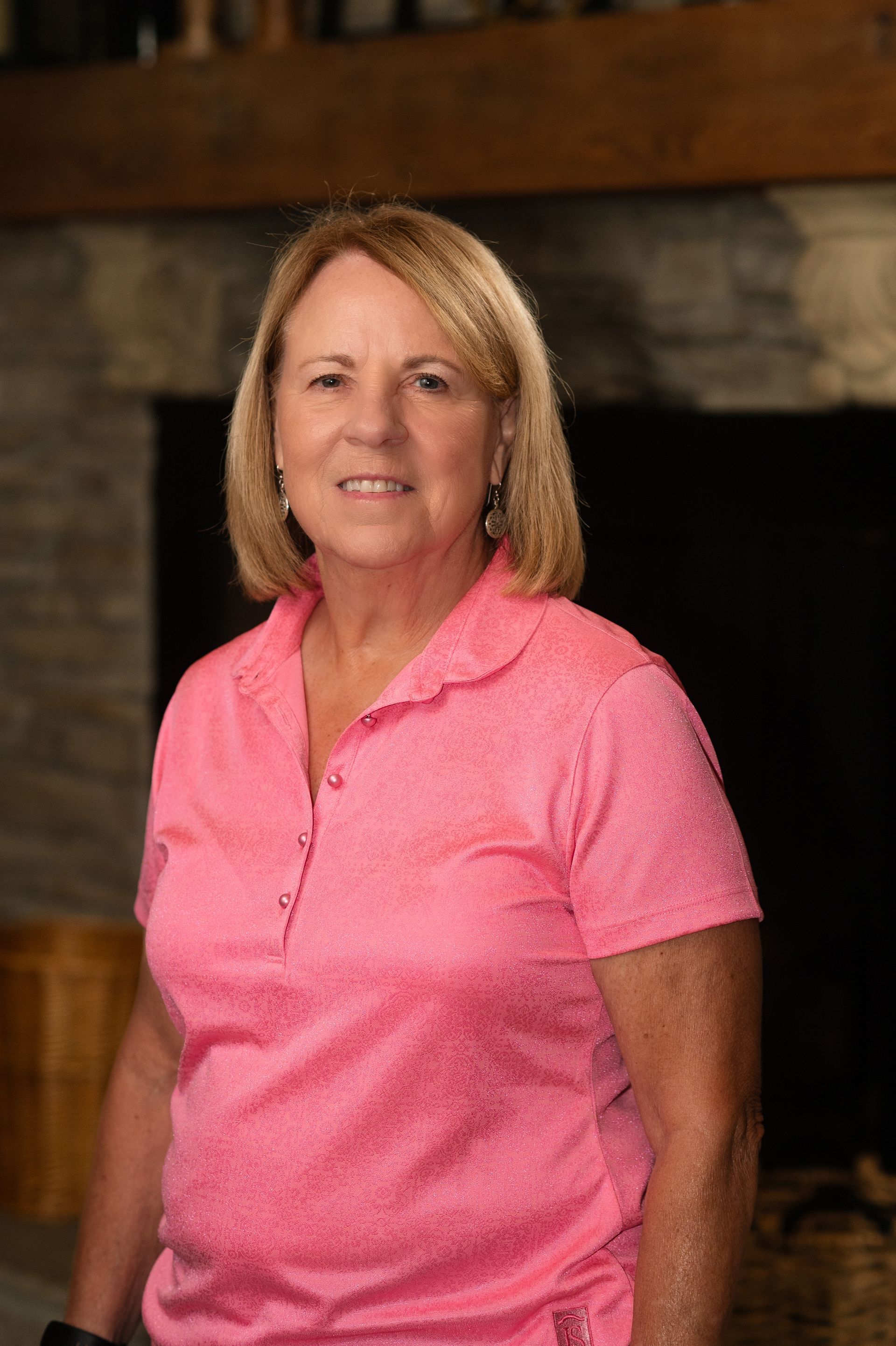 A woman in a pink shirt is standing in front of a fireplace.