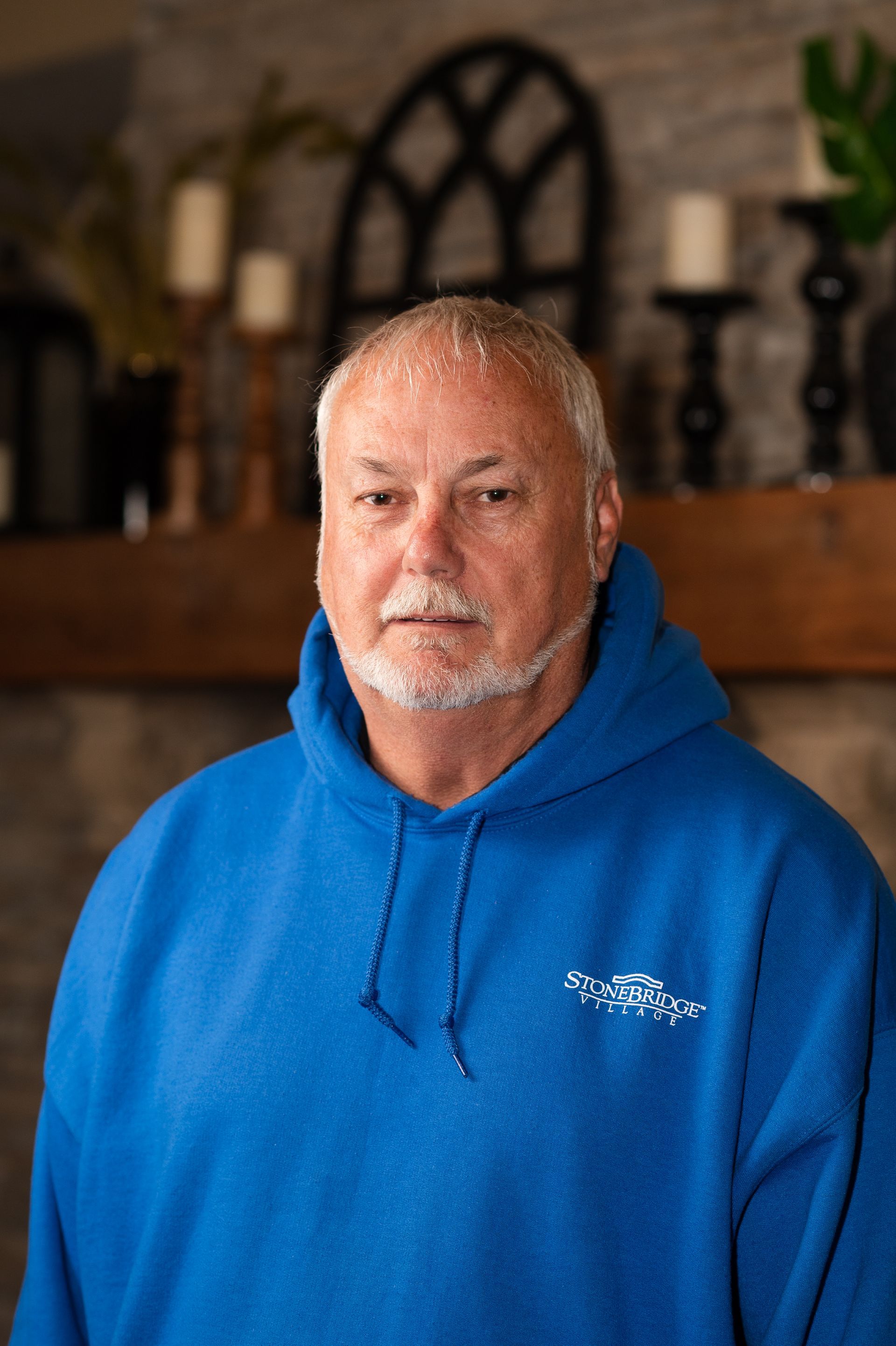 A man in a blue hoodie is standing in front of a fireplace.