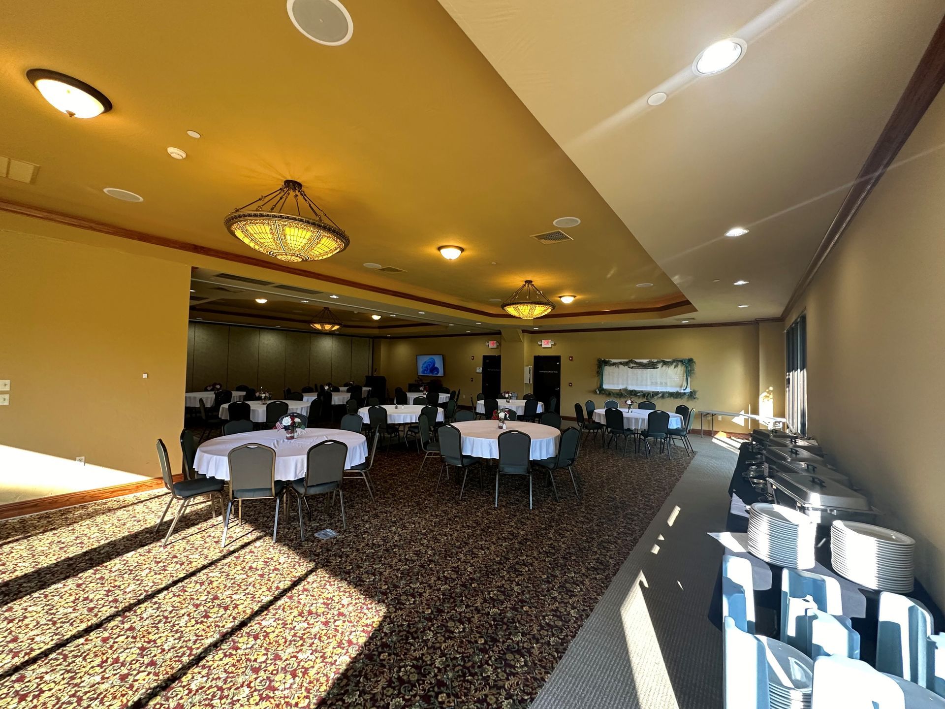 Spacious banquet hall with set tables, chairs, and warm ceiling lights casting shadows on the carpet.