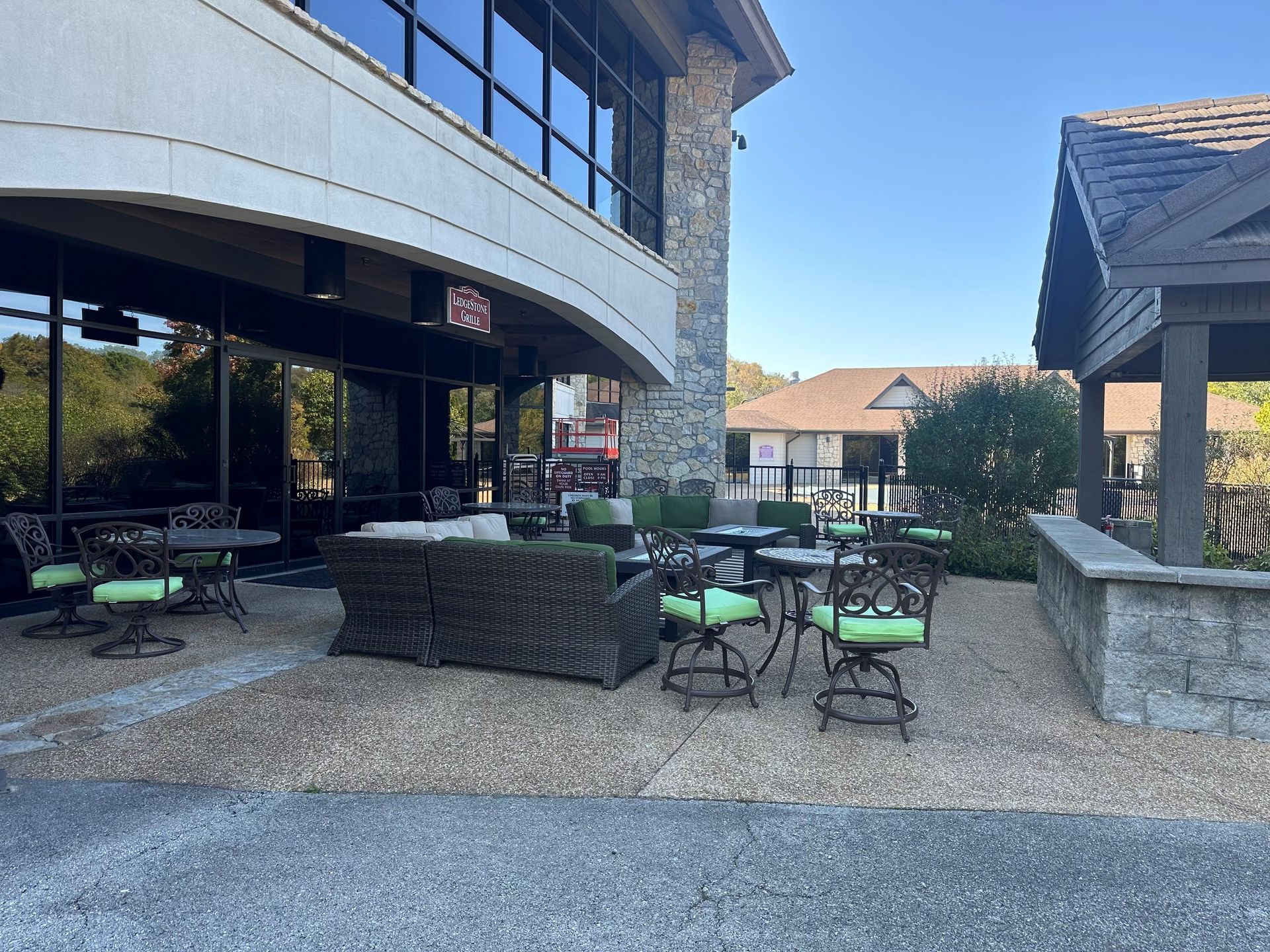 Outdoor patio with tables, green chairs, and wicker seating beside a modern building under a clear sky
