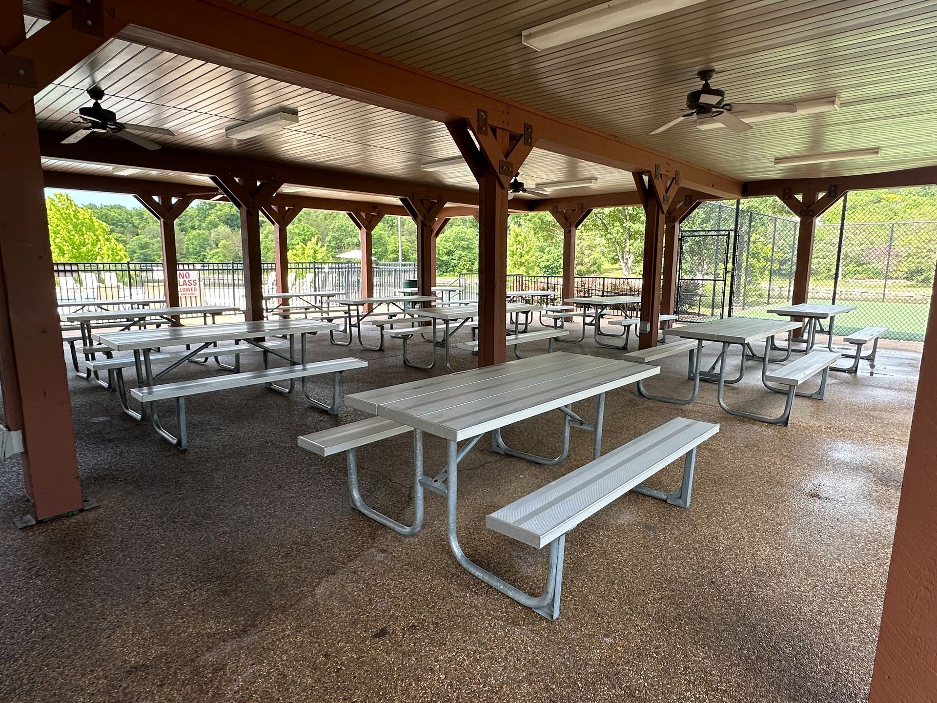 Covered picnic shelter with metal tables and benches on a wet floor, open to a park with trees.