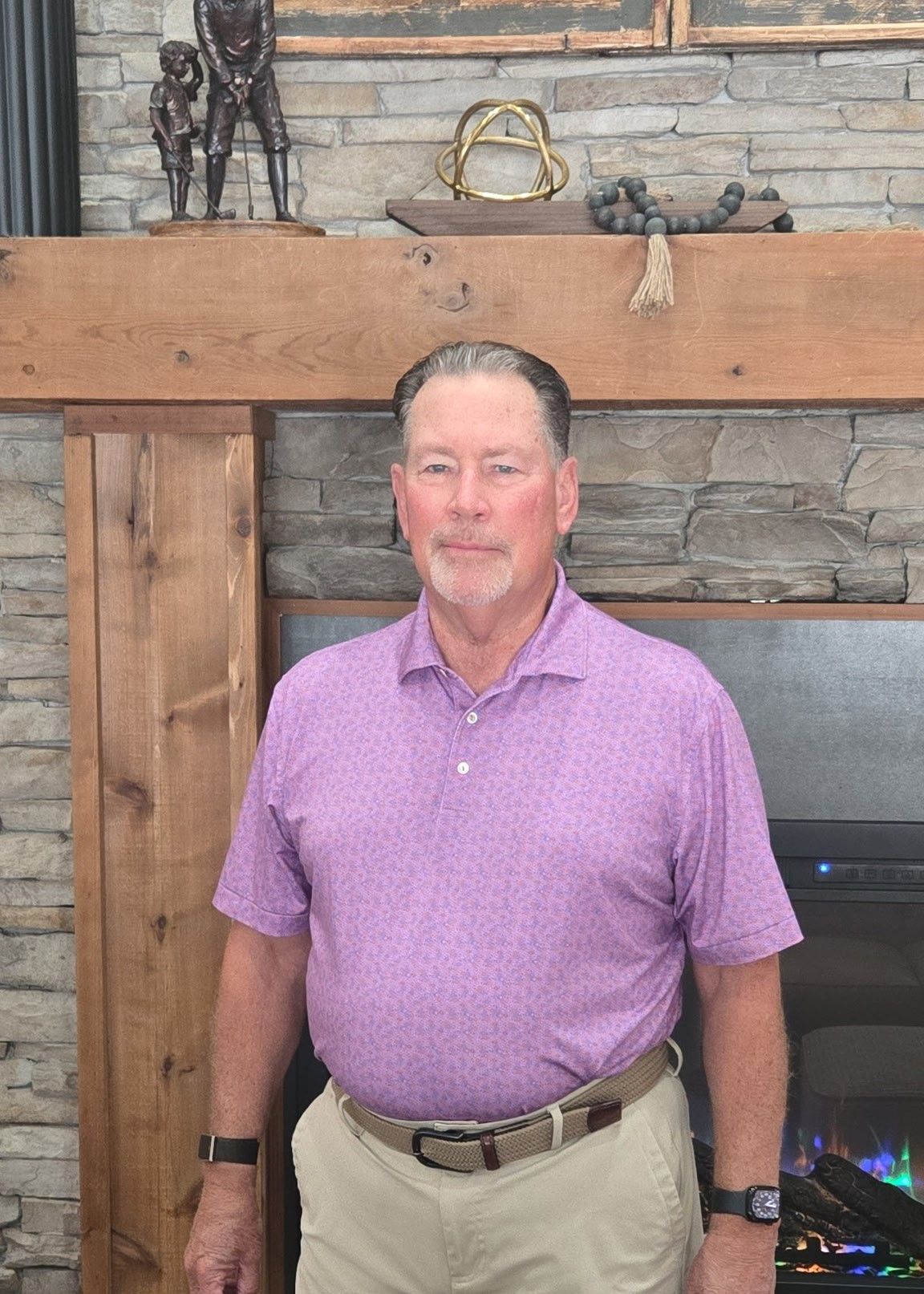 A woman in a pink shirt is standing in front of a fireplace.