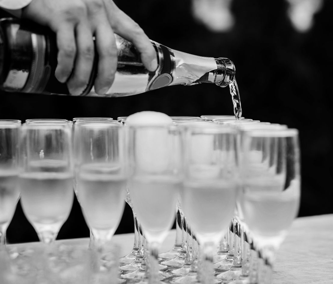 A person is pouring champagne into a row of wine glasses.