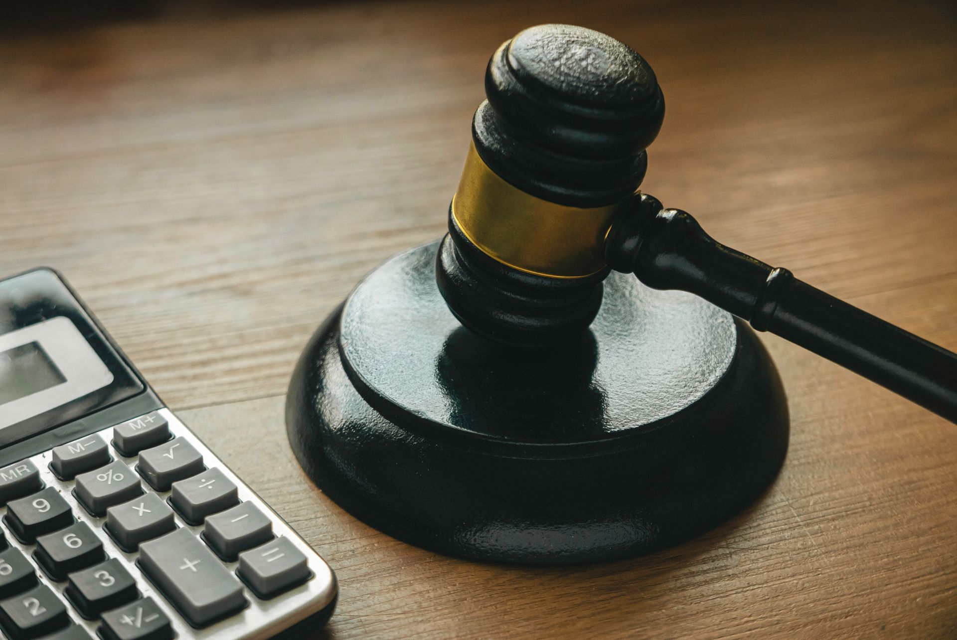 Photograph showing a black wooden judge's gavel resting on its sound block next to a gray calculator