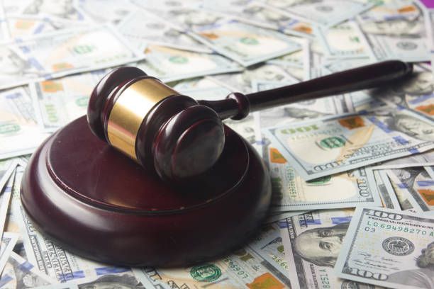 Gavel on wooden block atop a pile of scattered US hundred-dollar bills.