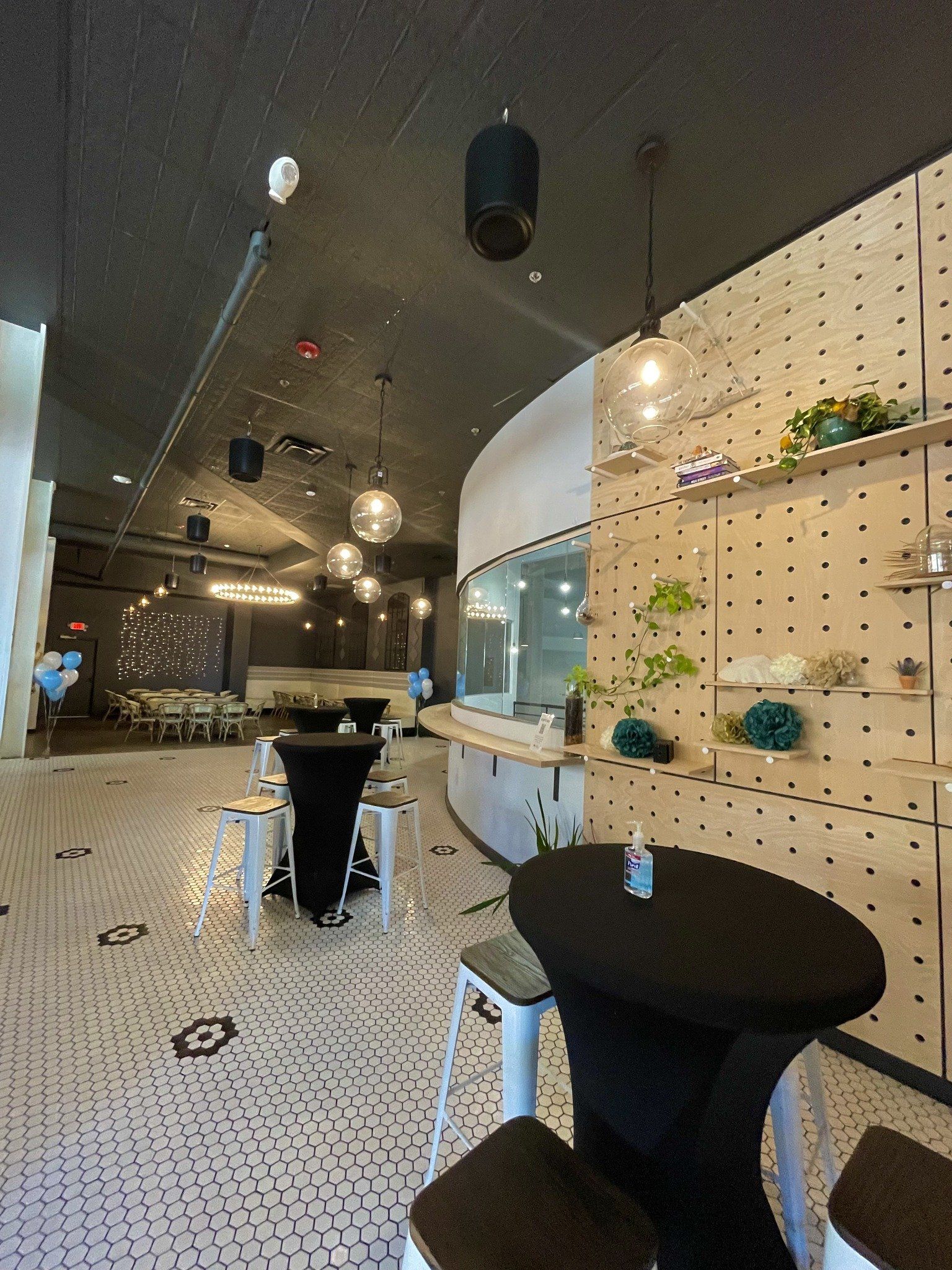 A restaurant with tables and stools and a bottle of hand sanitizer on the table