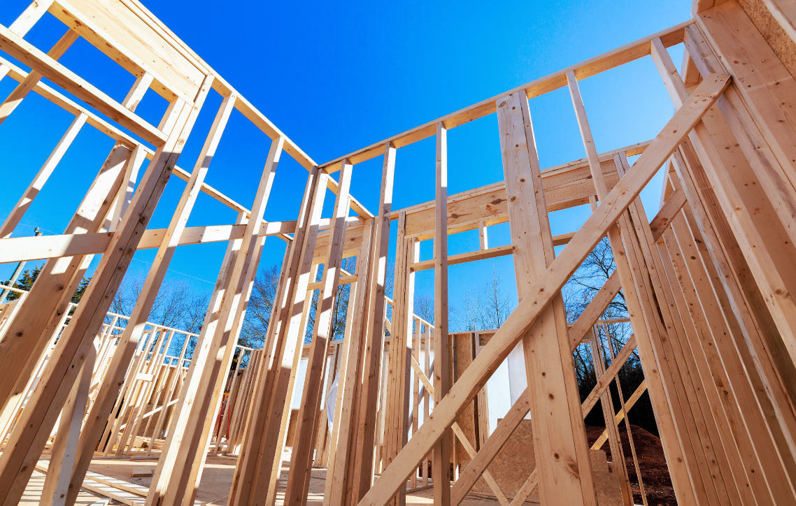 Framed wooden house under construction against a bright blue sky