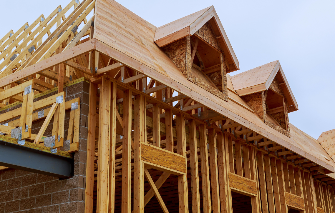Wood-frame house under construction with exposed beams and roof trusses
