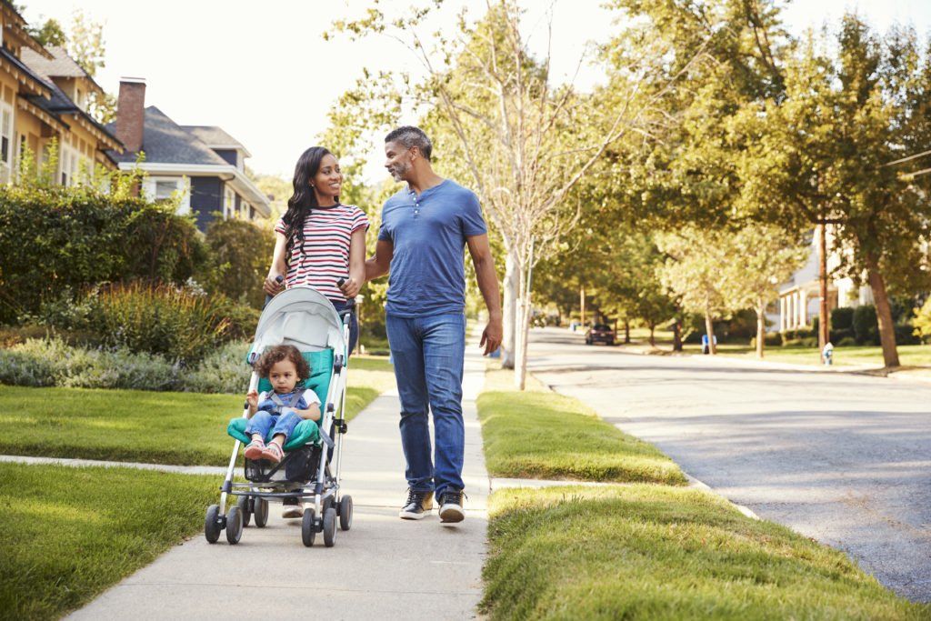A family is walking down the sidewalk with a baby in a stroller.