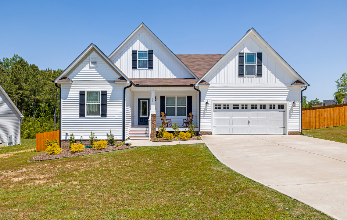 White suburban house with a two-car garage, front porch, and curved driveway on a sunny day
