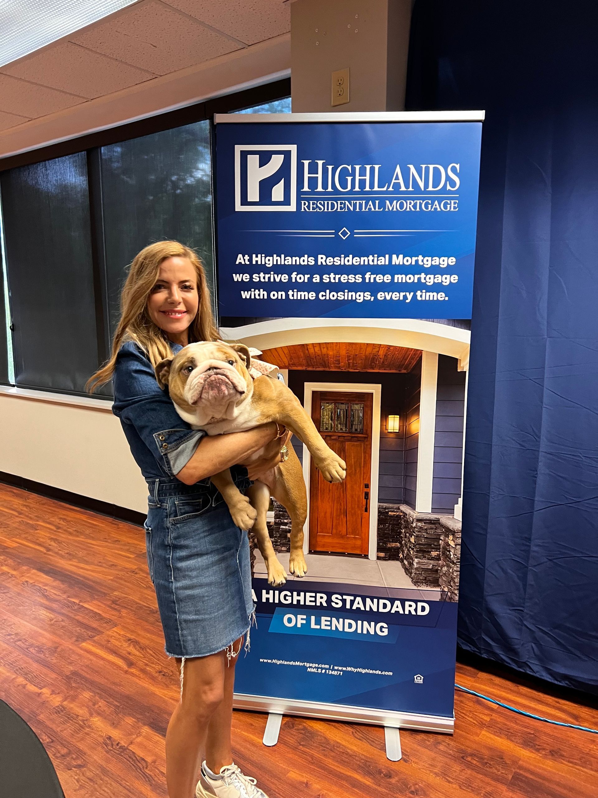 A woman holding a dog in front of a highlands sign