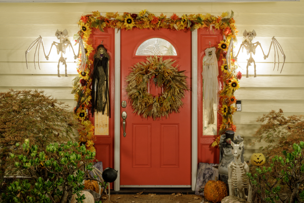 A red door with a wreath on it is decorated for halloween
