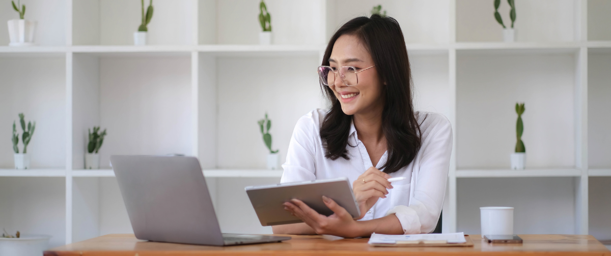 A woman is sitting at a desk with a laptop and a tablet.