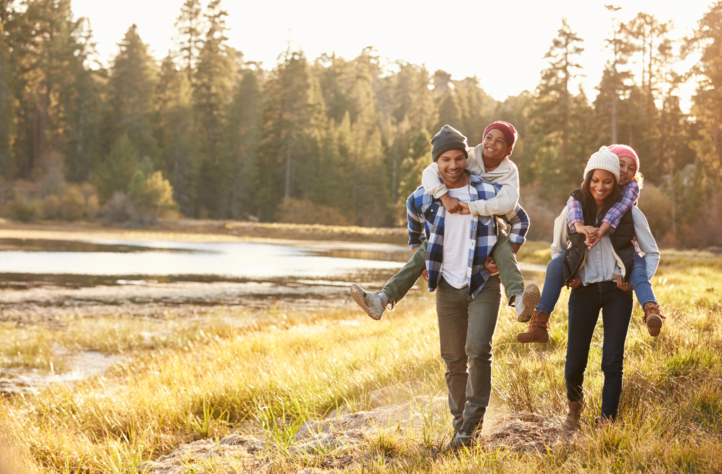 A family is walking in a field with a man carrying two children on his shoulders.