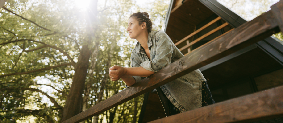 A woman is leaning on a wooden railing of a tree house.