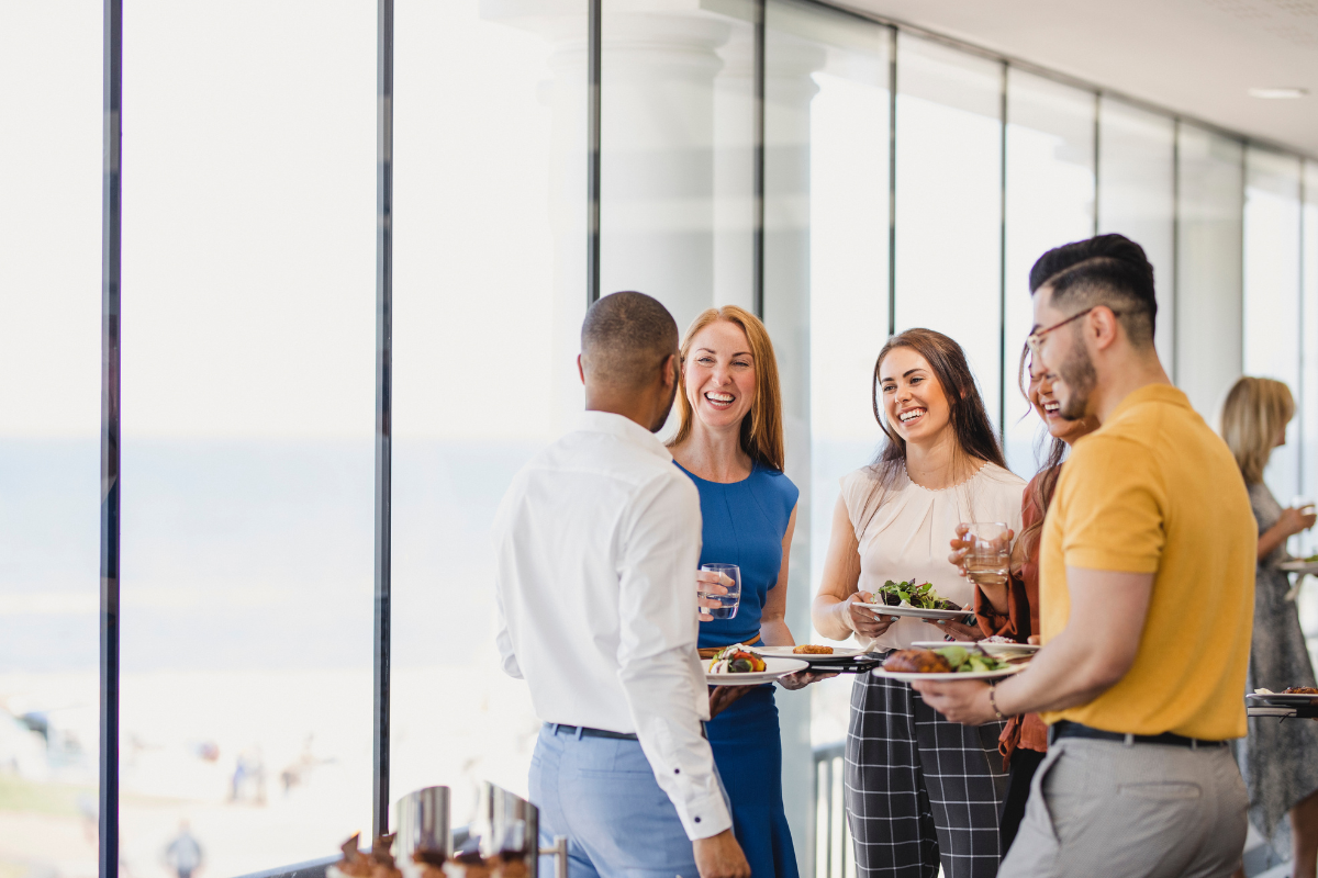 A group of people are standing in front of a window holding plates of food.