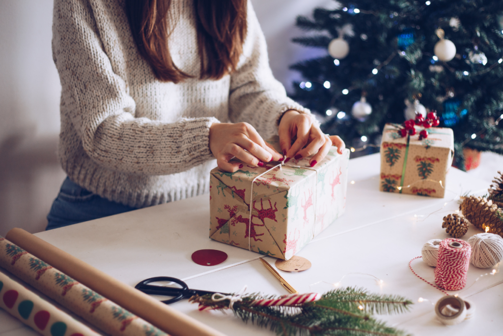 A woman is wrapping a christmas present in front of a christmas tree.