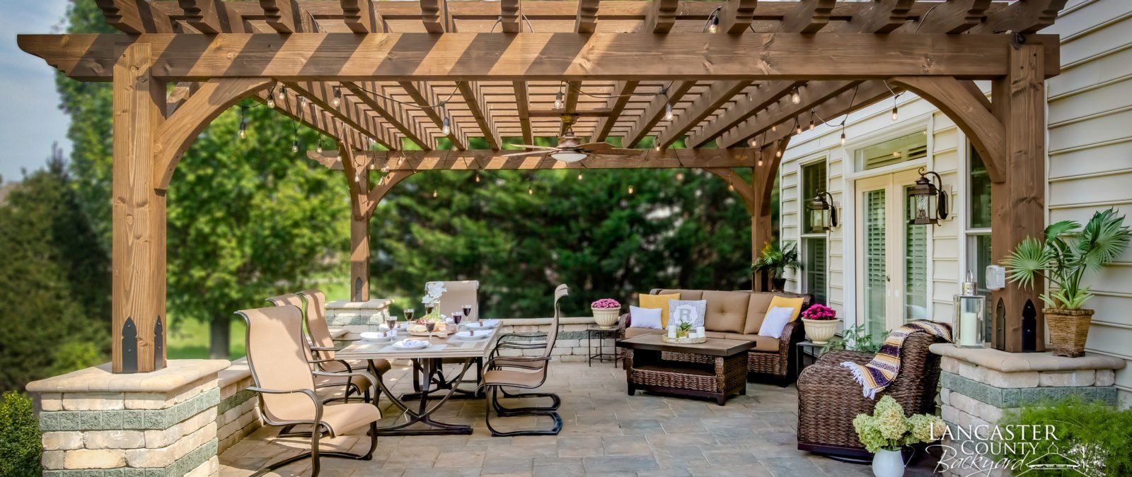 A wooden pergola over a patio with a table and chairs underneath it.