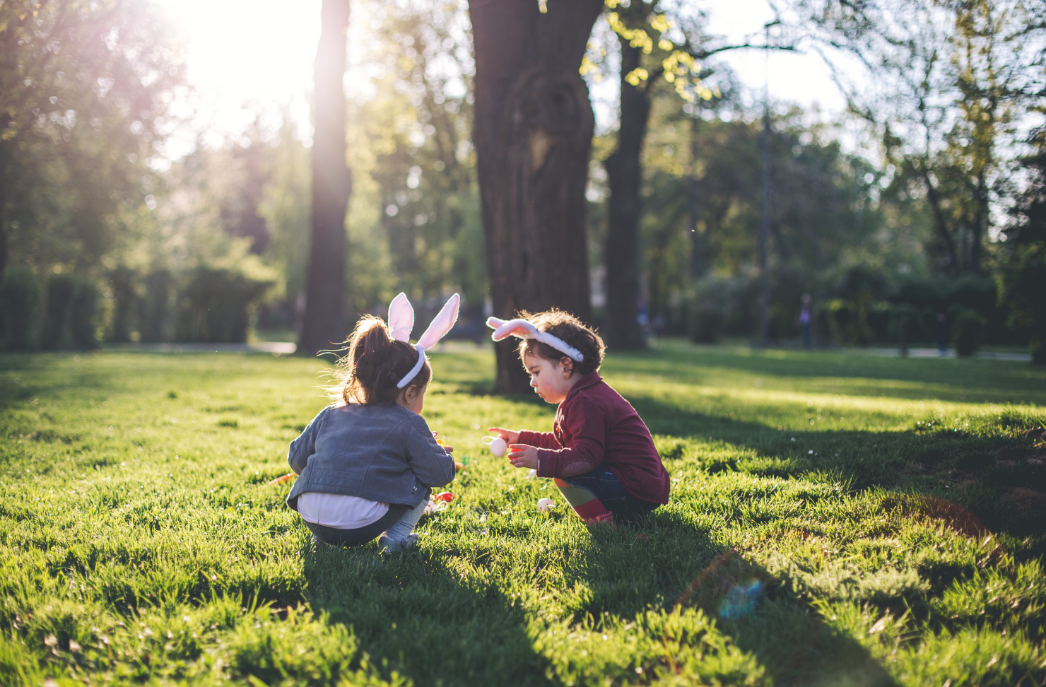 Two little girls wearing bunny ears are playing in the grass.