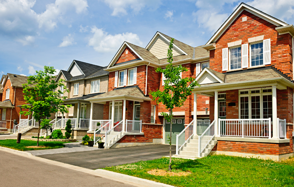 Row of suburban brick houses with porches, white trim, and green lawns under a blue sky