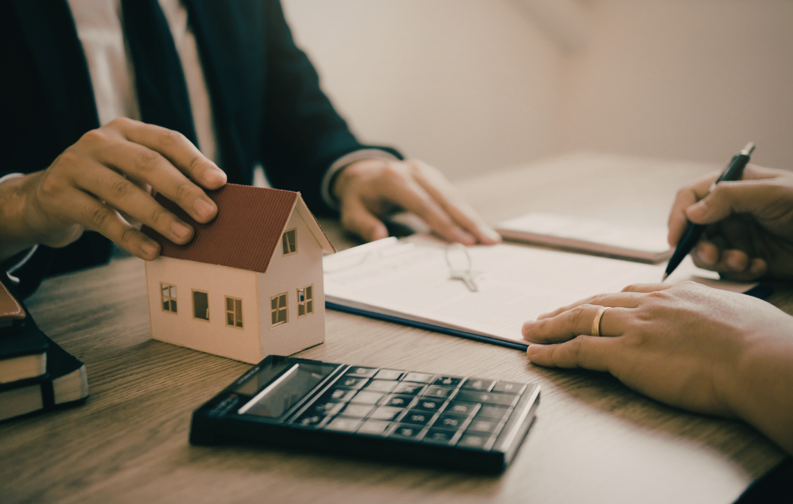 Hands reviewing a house model with calculator and documents during a real estate meeting