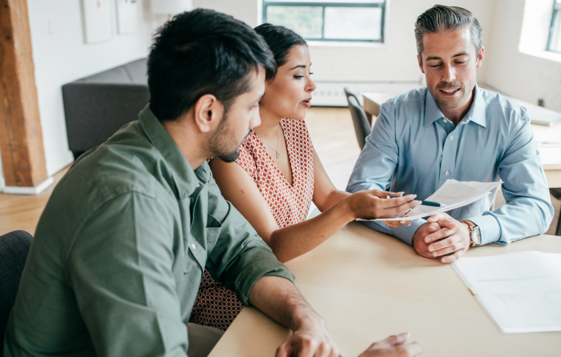 Three people in a meeting talking around a table with documents