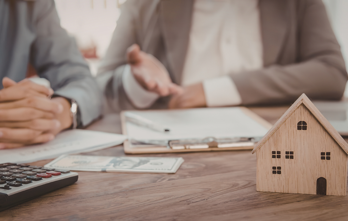 Hands reviewing paperwork beside a calculator and small house model on a wooden table