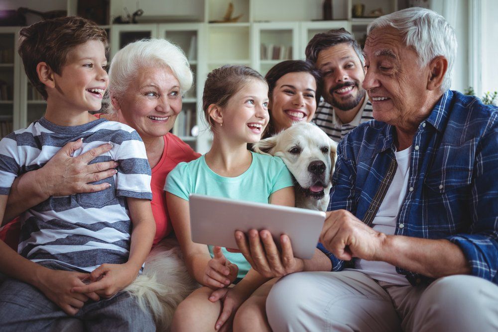 A family is sitting on a couch looking at a tablet.