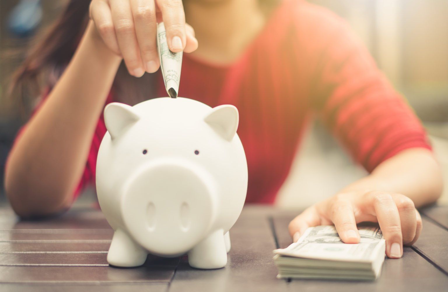 A woman is putting a dollar bill into a piggy bank