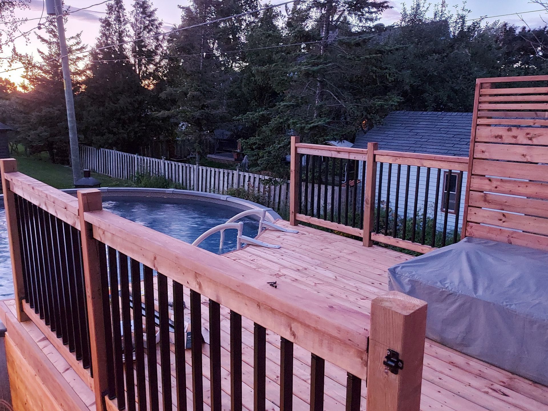 A wooden deck with a hot tub and a pool in the background