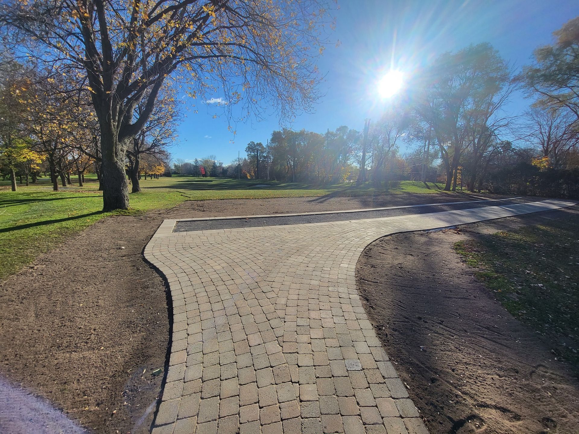 A brick walkway leading to a park on a sunny day.