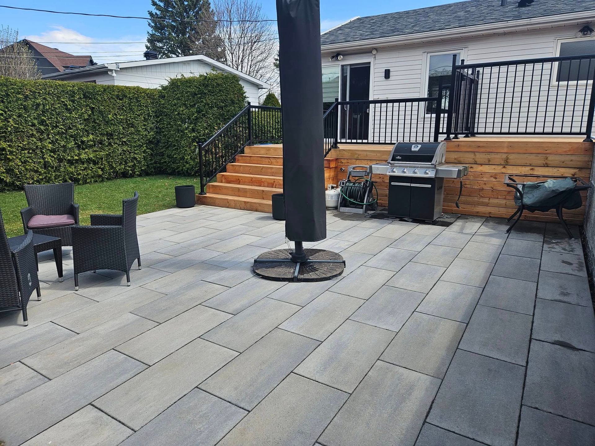A patio with a grill and umbrella in front of a house.