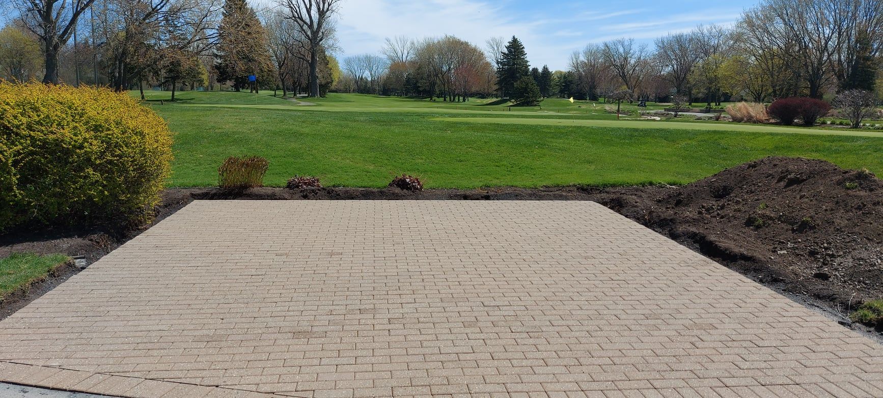 A brick driveway leading to a golf course with trees in the background.