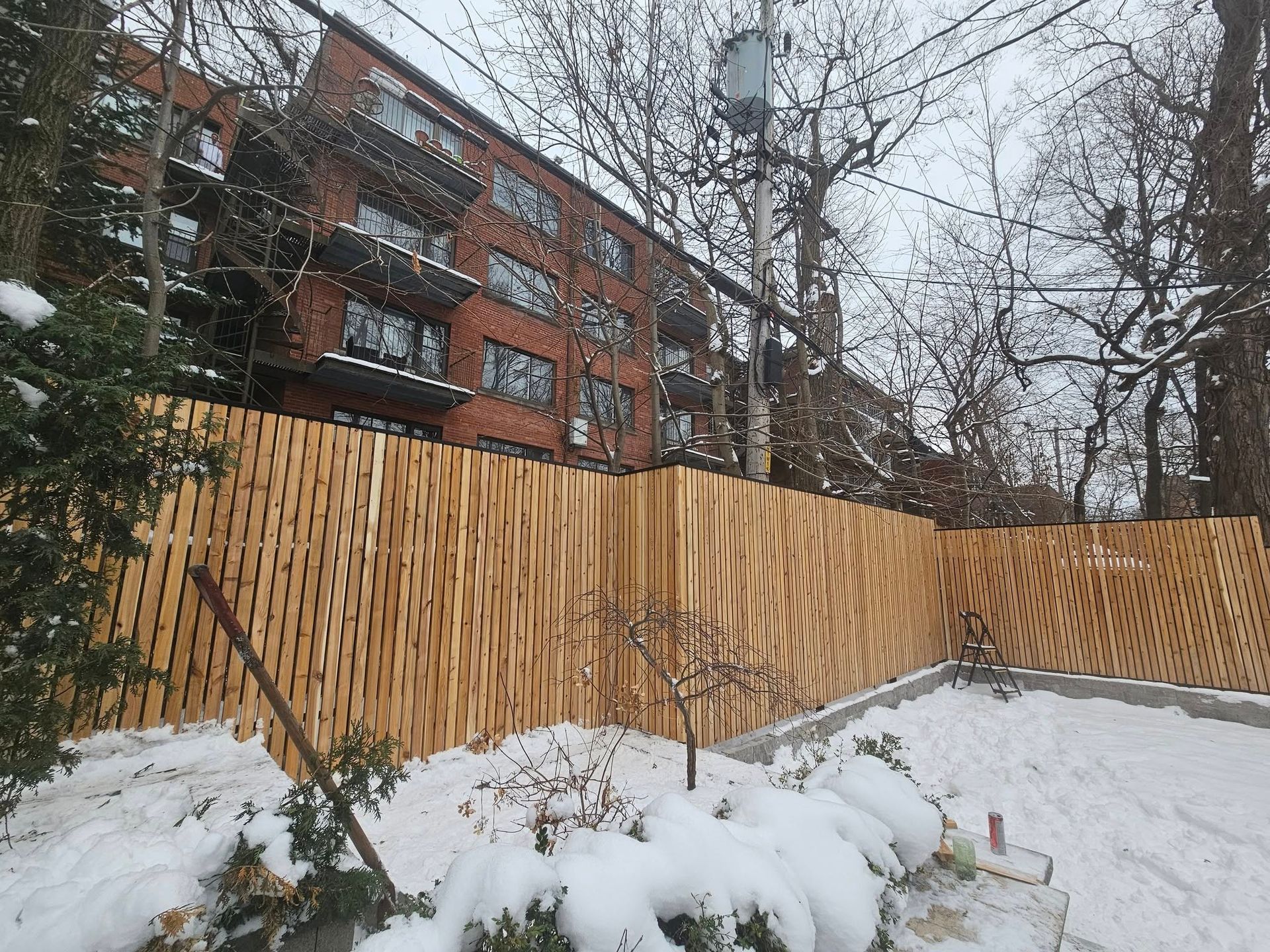 A wooden fence is surrounded by snow in front of a building.