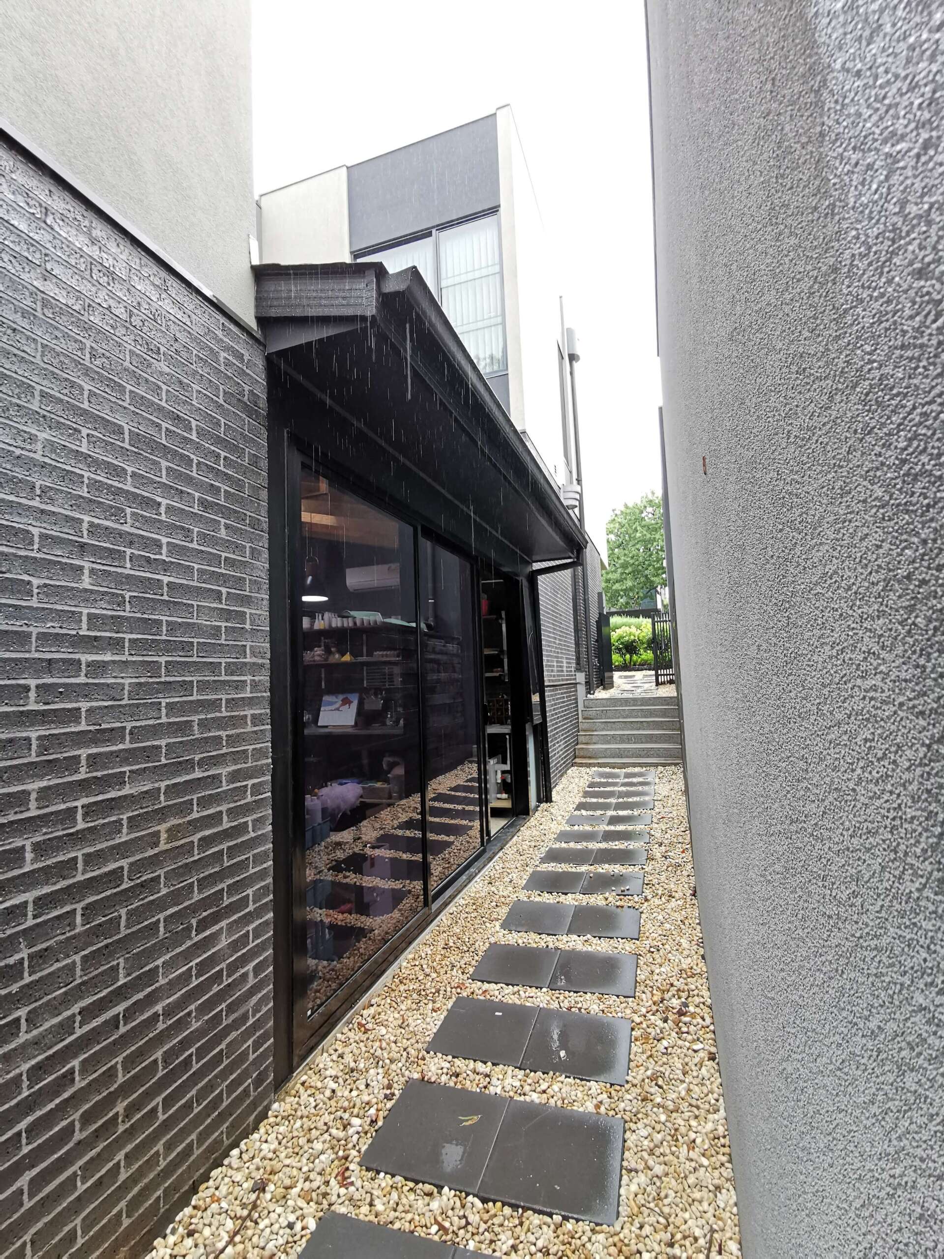 A narrow walkway between two buildings with brick walls and gravel.