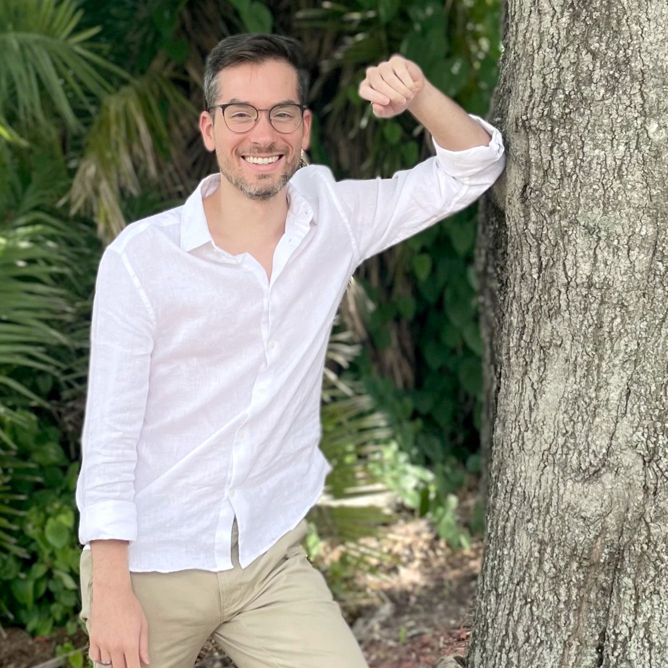 A man in a white shirt is leaning against a tree