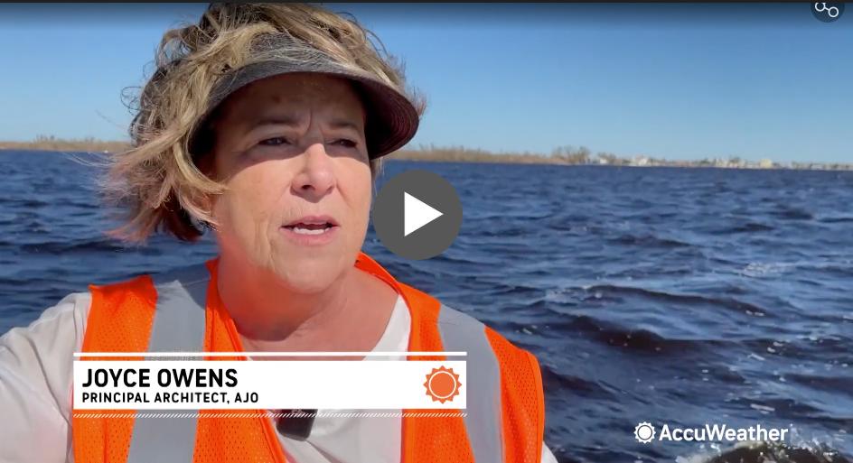 A woman in an orange vest and hat is standing in the water. Architecture Joyce Owens