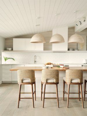 A kitchen with white cabinets , a large island , and wicker bar stools.