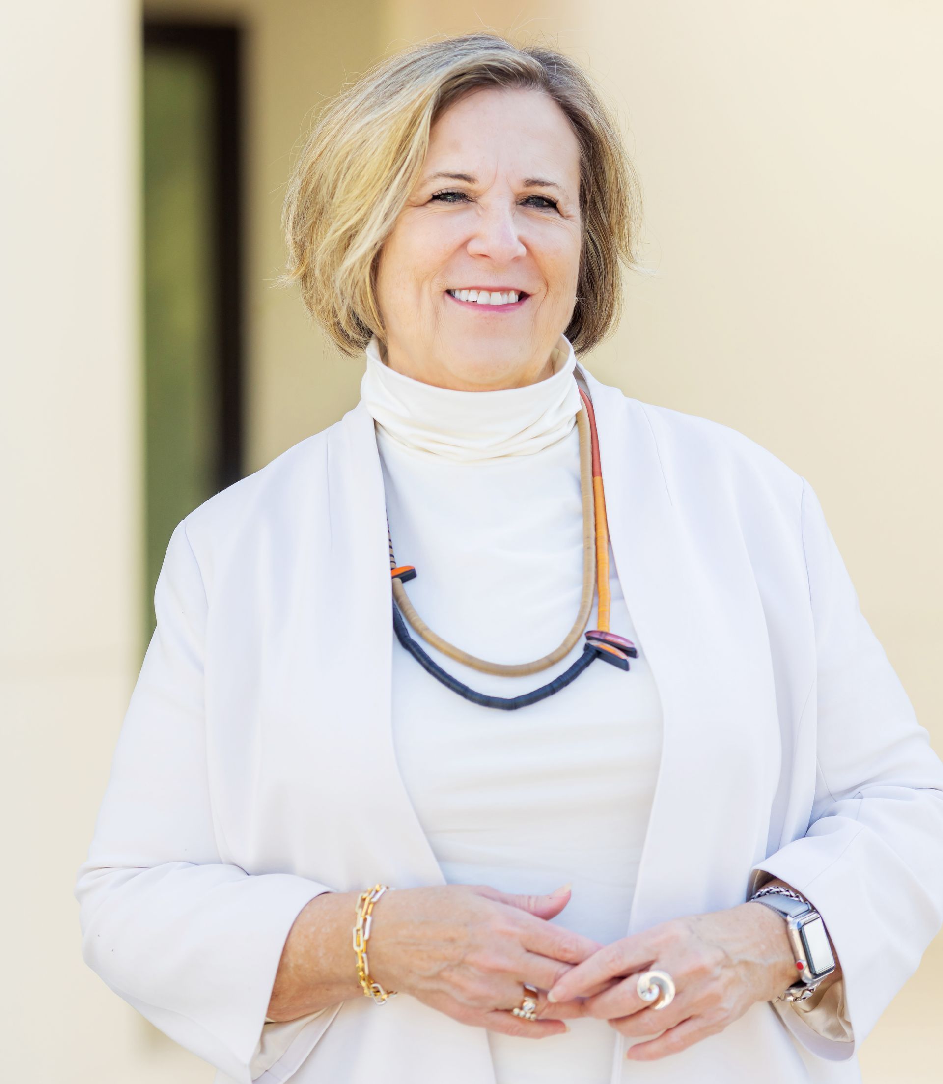 A woman wearing a white jacket and a necklace is smiling for the camera.