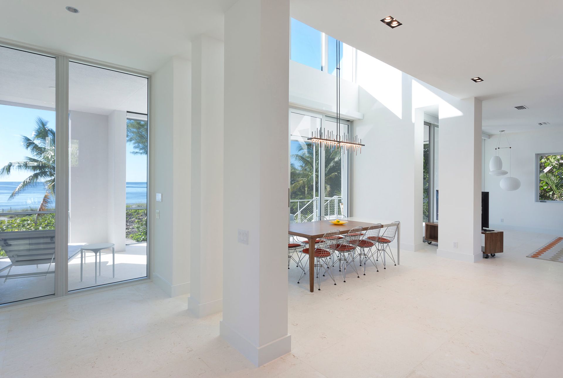 a white dining room with a table and chairs and large windows with a view of the ocean