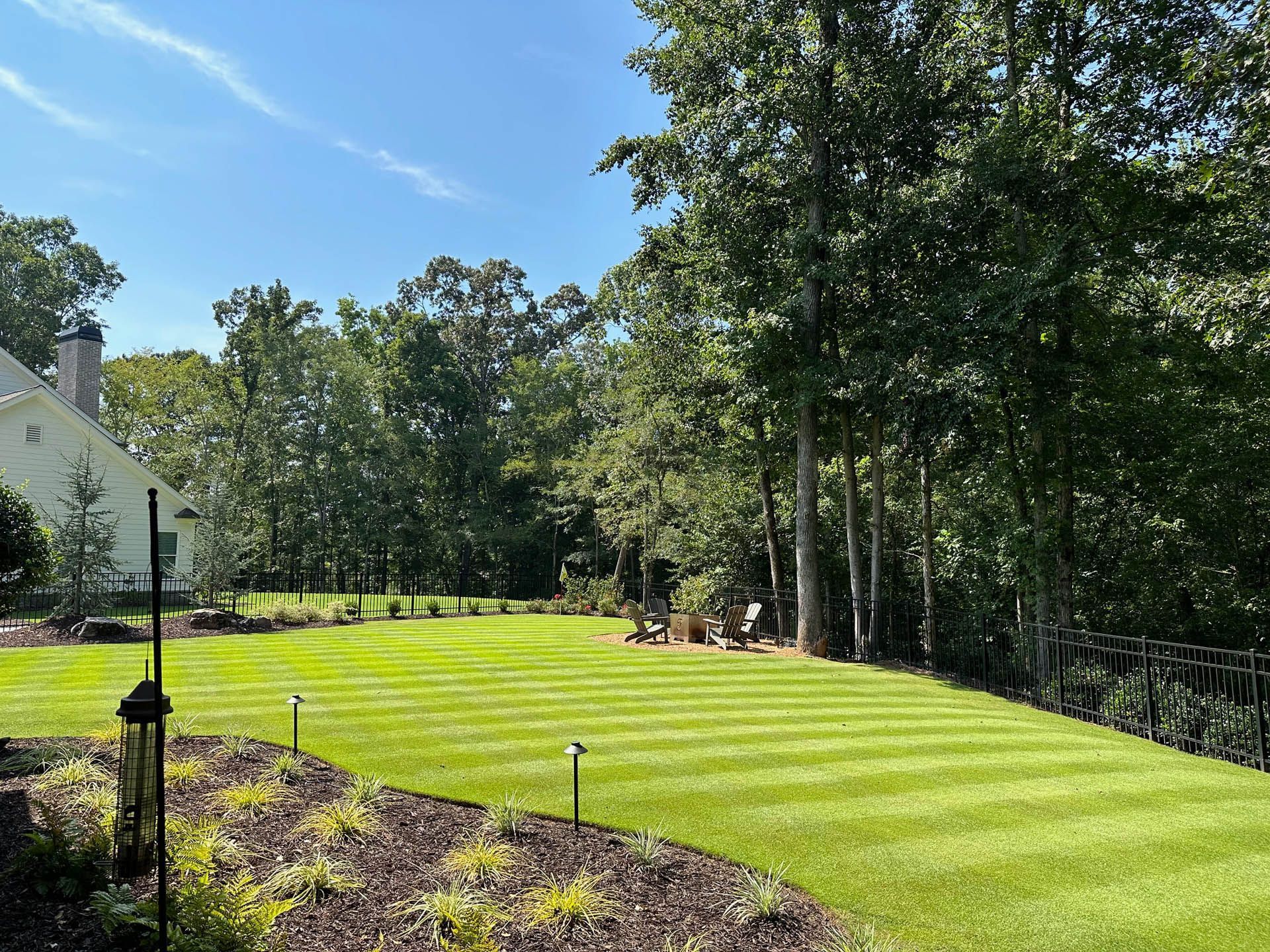 A large lush green lawn with trees in the background and a house in the background.