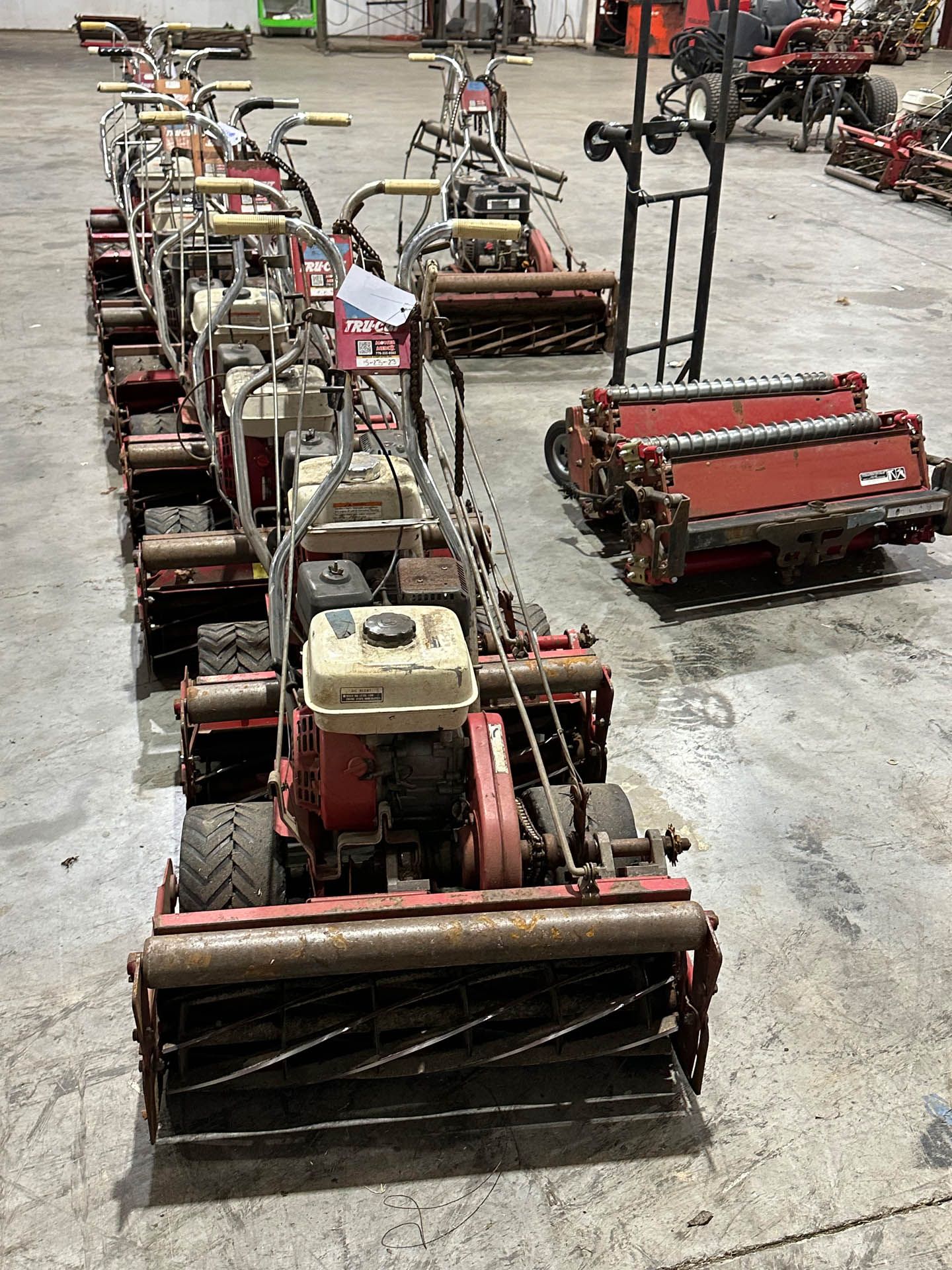 A row of lawn mowers are lined up in a warehouse.