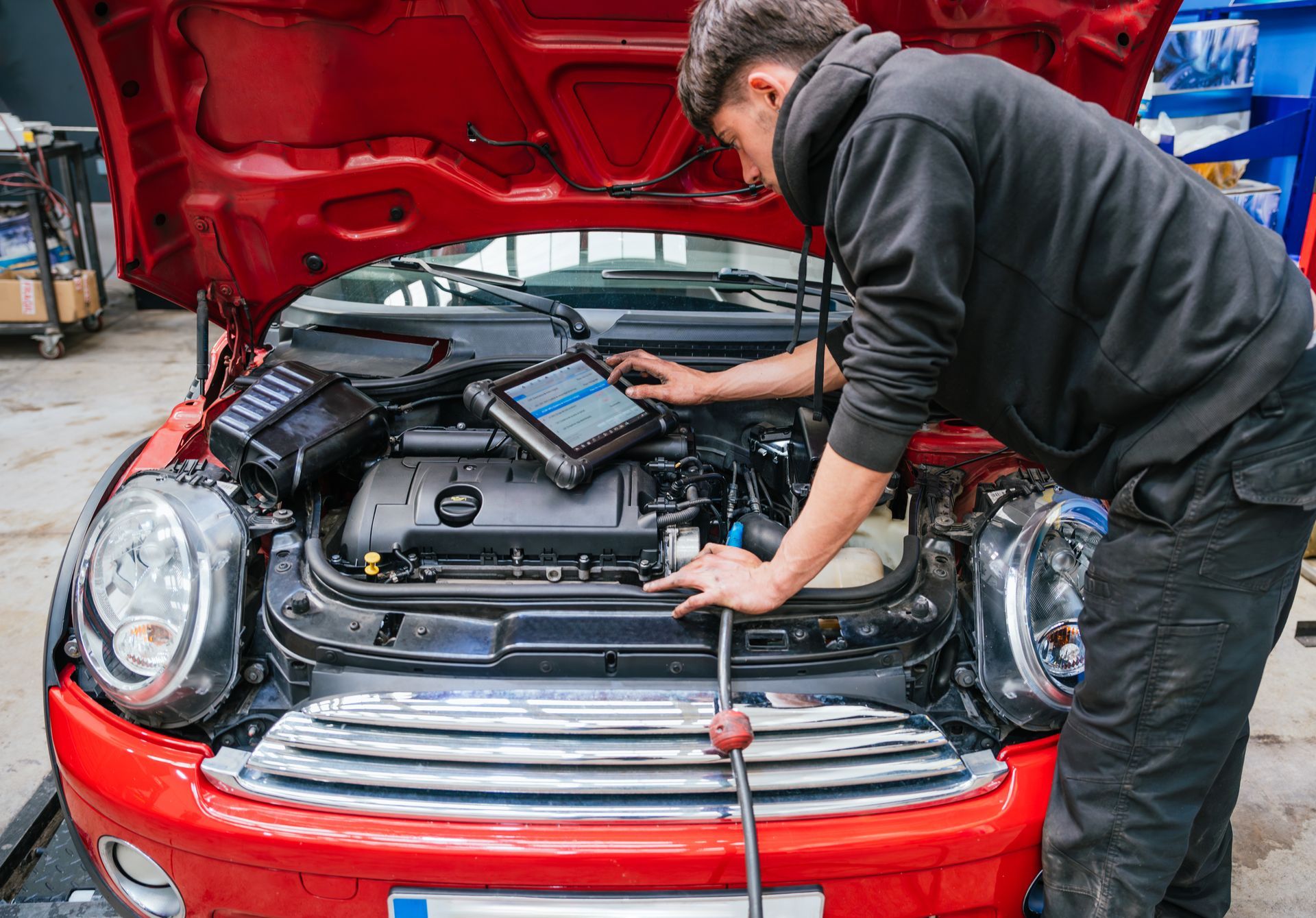 Mechanic working under the hood of a red car in a garage, with diagnostic equipment open.