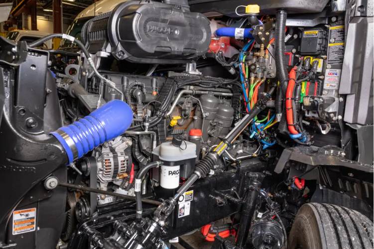 Truck cab interior with exposed engine, wiring, and blue hose in a repair setting