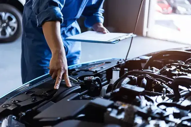 Person inspecting an open car engine in a garage