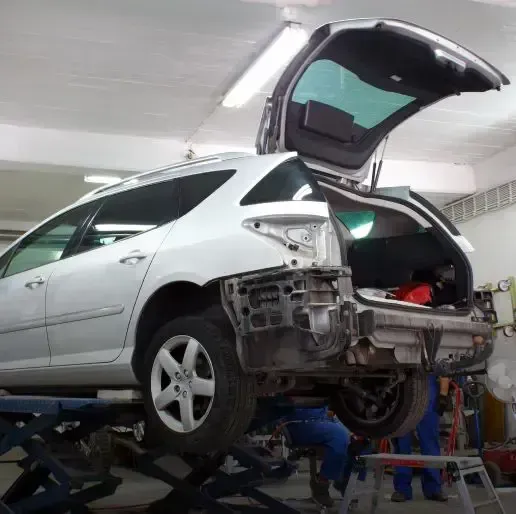 Silver hatchback on a repair lift with rear bumper removed in an auto body shop