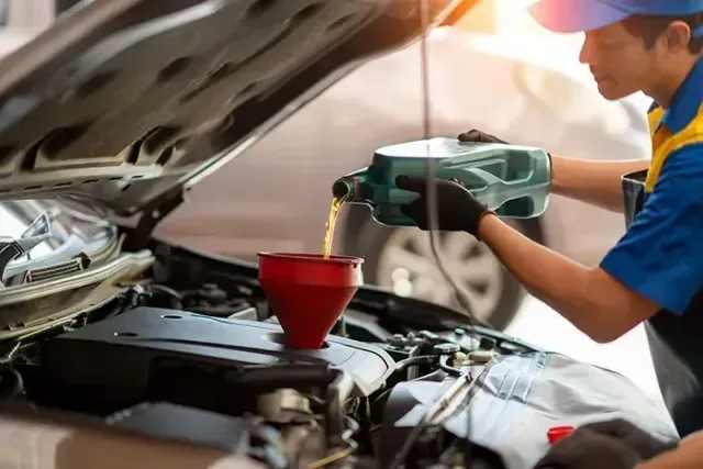 Mechanic pouring oil into a car engine with a green container in an auto repair shop